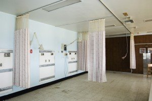 Empty hospital room with blue walls curtains and wall lamps
